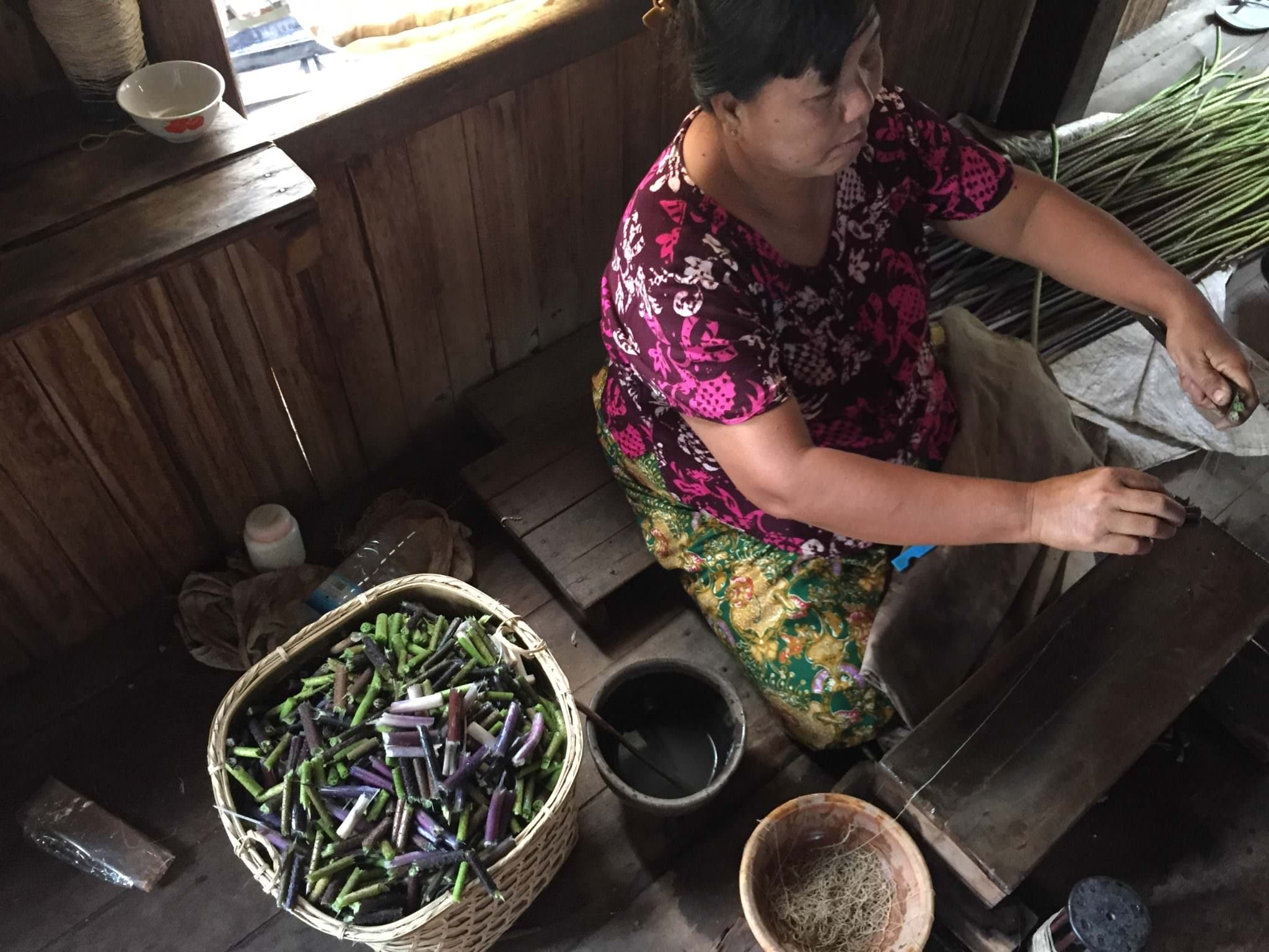 A basket of lotus stems sits beside a woman extracting their fibers. © 2015 Gail Jessen